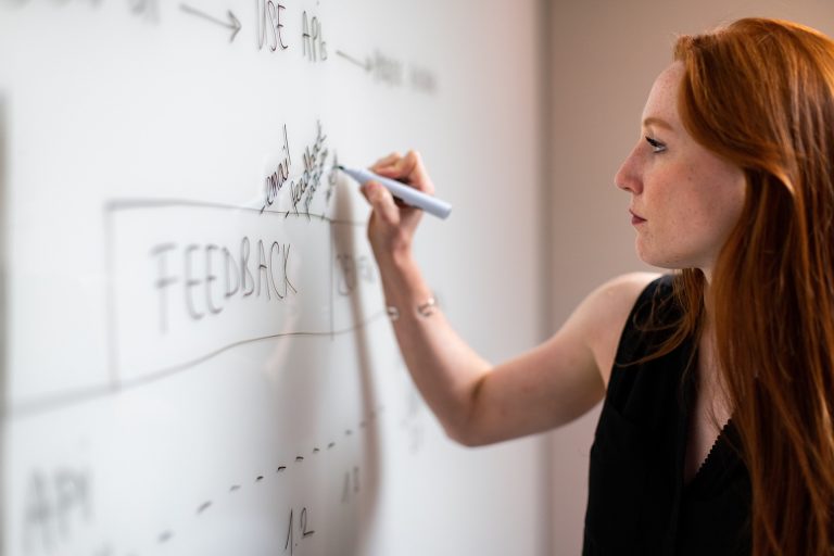 A woman using a dry erase marker on a whiteboard at her field service job.