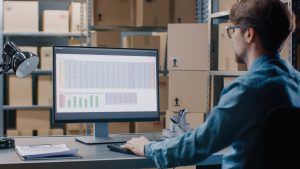 A logistics professional analyzing a complex spreadsheet and charts on a computer screen to monitor vendor lead time data.