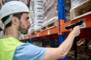 Warehouse worker scanning a lot number label on a storage rack for lot and serial tracking