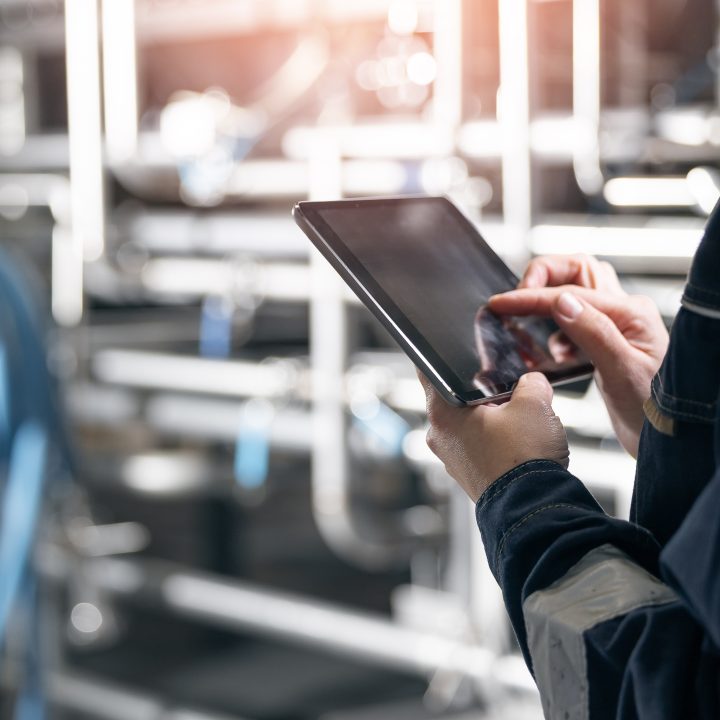 A worker using a digital tablet to record data during an annual physical inventory count in an industrial manufacturing plant.