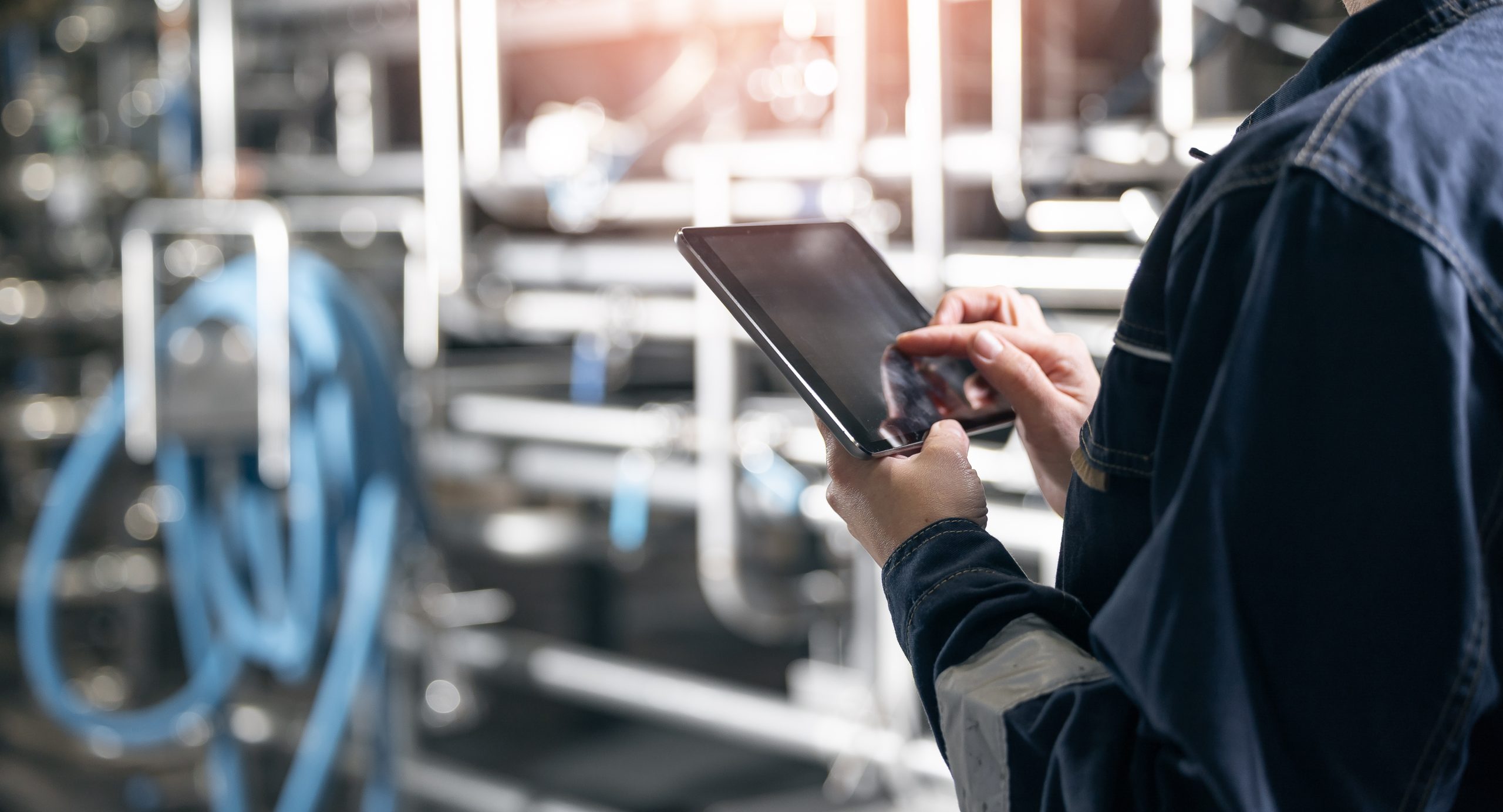 A worker using a digital tablet to record data during an annual physical inventory count in an industrial manufacturing plant.