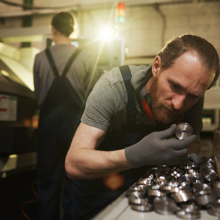 A focused factory worker examining small metal components closely, illustrating a detailed manual stock checking process.
