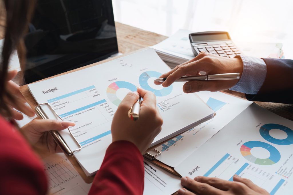 Two professionals pointing at financial charts and budget spreadsheets to finalize a yearly inventory valuation report.